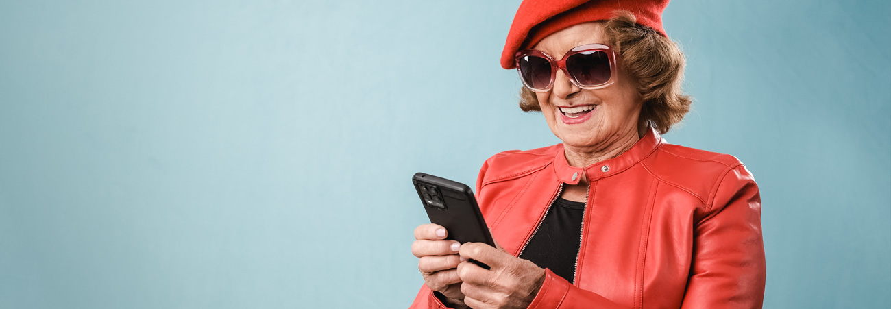 Coole Senioren mit roter Mütze schaut lachend ins Smartphone