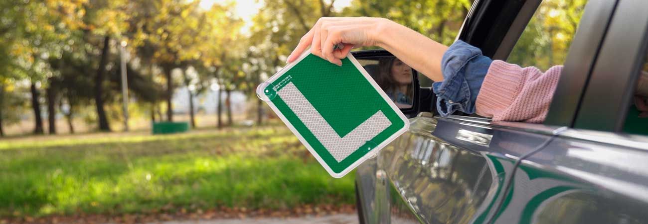Hand hält grünes L-Schild aus dem Autofenster – Symbol für begleitendes Fahren und erste Fahrpraxis