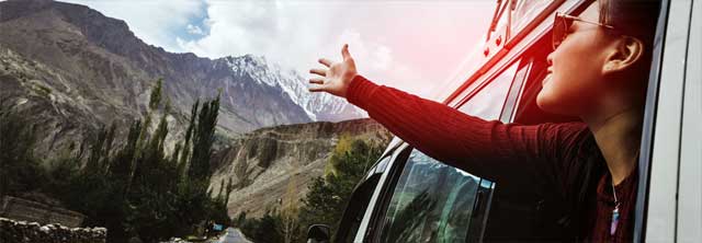 Frau hält Hand aus dem Auto und begrüßt symbolisch die Berge