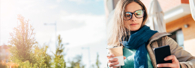 Frau mit Kaffee und Smartphone in der Hand