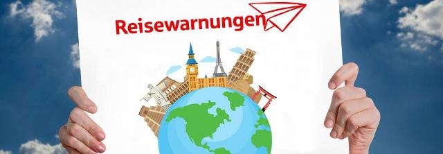 Schild mit Hinweis Reisewarnung vor Sommerhimmel