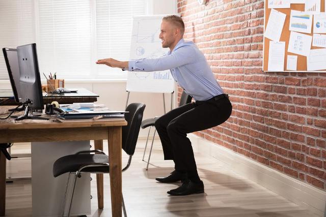 Junger Mann macht Gymnastikuebungen im Büro 