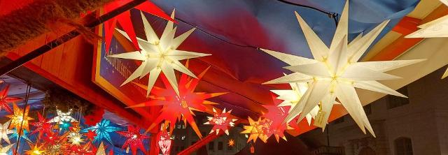 Leuchtende Weihnachtssterne hängen an einem Verkaufsstand auf dem Weihnachtsmarkt