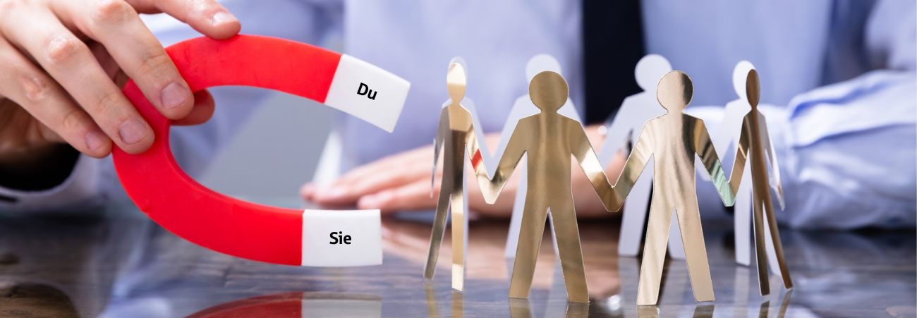 Geschäftsmann zieht Menschen aus Pappe mit Hufeisenmagnet mit den Polen Sie und Du an