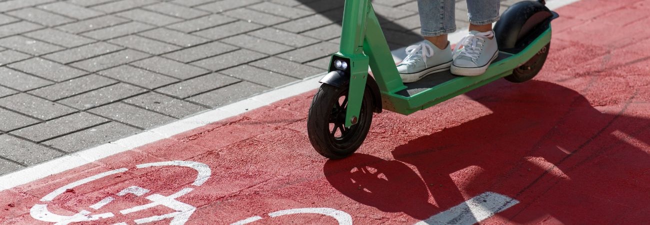 Zwei Füße auf einem grünen E-Scooter, der auf einen rotem Radweg fährt