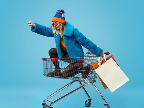 Bildmontage: Junge Frau mit Einkaufstüten sitzt in einem Einkaufswagen