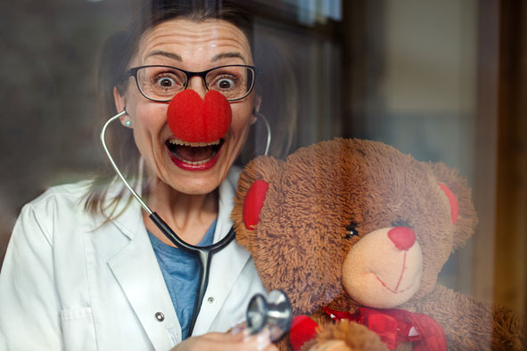 lachender Klinikclown mit Teddybär