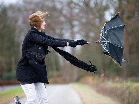 Frau im Sturm mit Regenschirm der fast davonfliegt