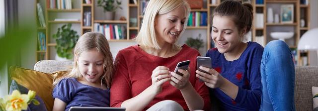 Frau spielt mit ihren zwei Töchtern am Smartphone